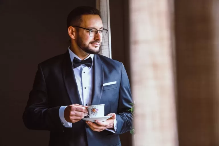 Przygotowania pana młodego. Zamyślony pan młody z filiżanką kawy. rekwizyty w sesji ślubnej. Gra światła w zdjęciach pana młodego. Reportaż ślubny.