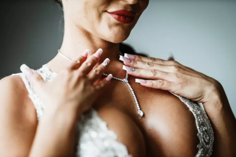 Panna młoda poprawia kolię, którą ma zawierzoną na szyi. Zdjęcie detalu akcesoriów ślubnych panny młodej.
