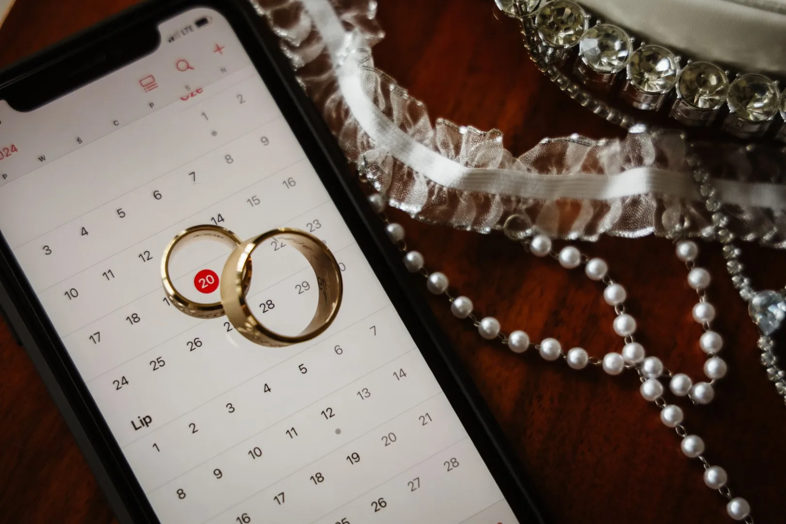 Złote obrączki ślubne. Wyświetlona data ślubu na ekranie telefonu, obok ślubna biżuteria