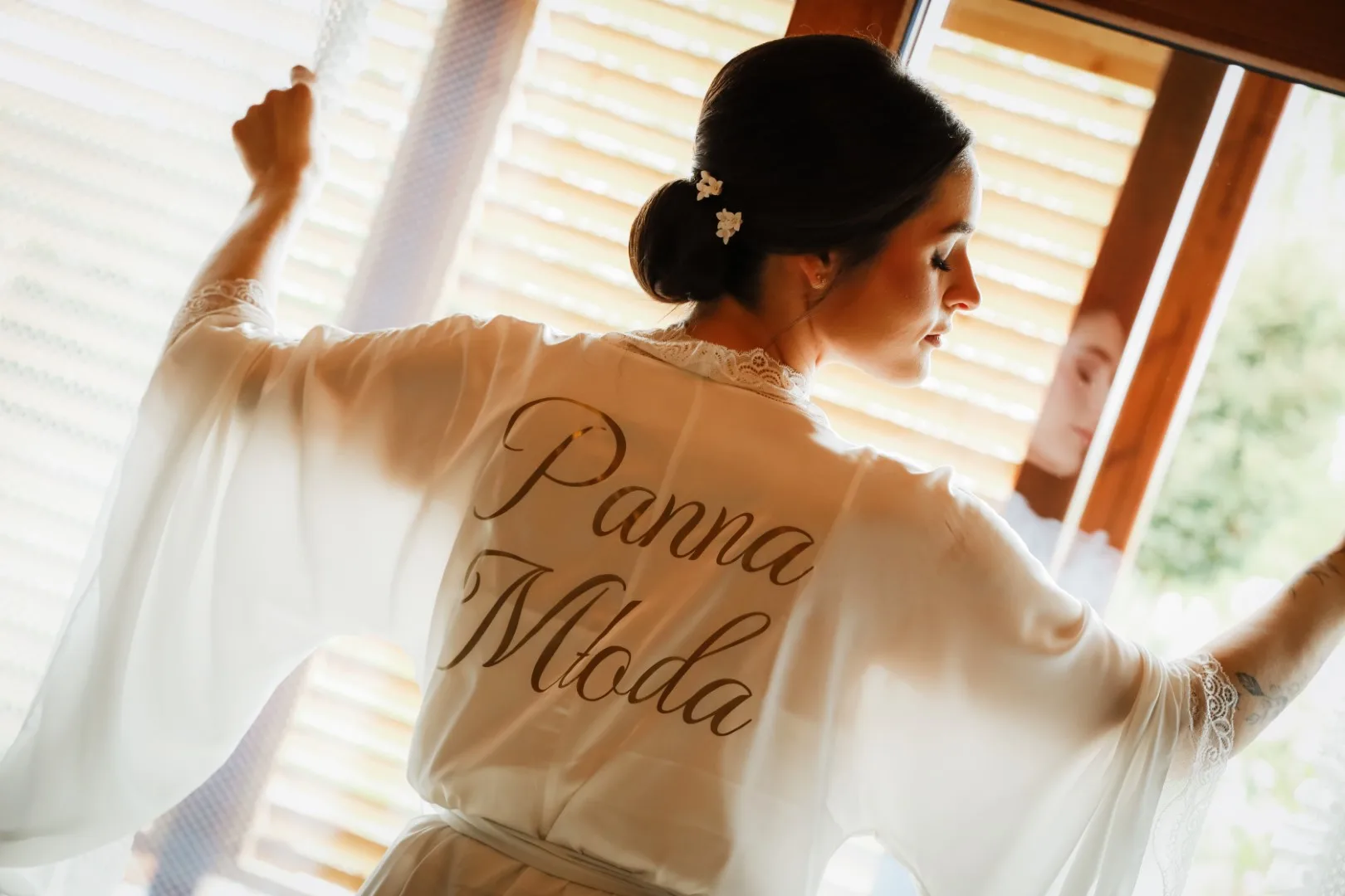 Panna młoda w białym jedwabnym szlafroku. Fotograf ślubny uchwycił Piękne światło wpadające przez okiennice i rozświetlające biały szlafrok