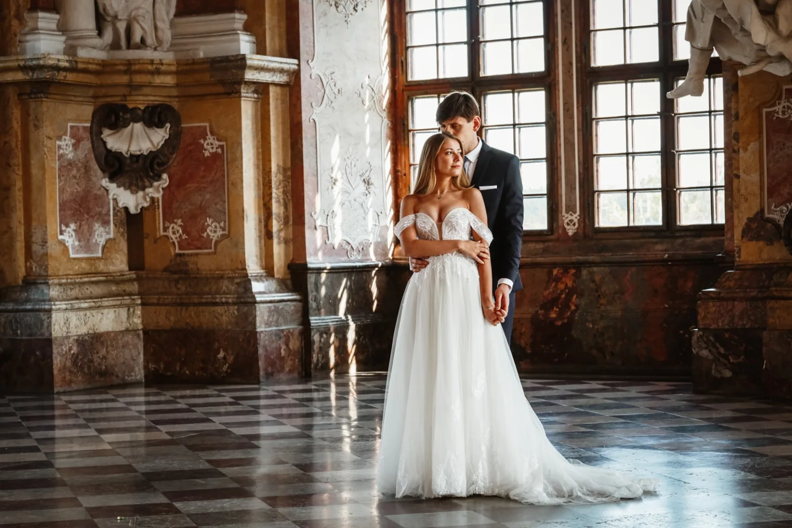 Panna Młoda w objęciach swego męża. Piękna biała suknia ślubna z rozłożystym trenem. Sesja w romantycznym klimacie i zamkowych wnętrz.